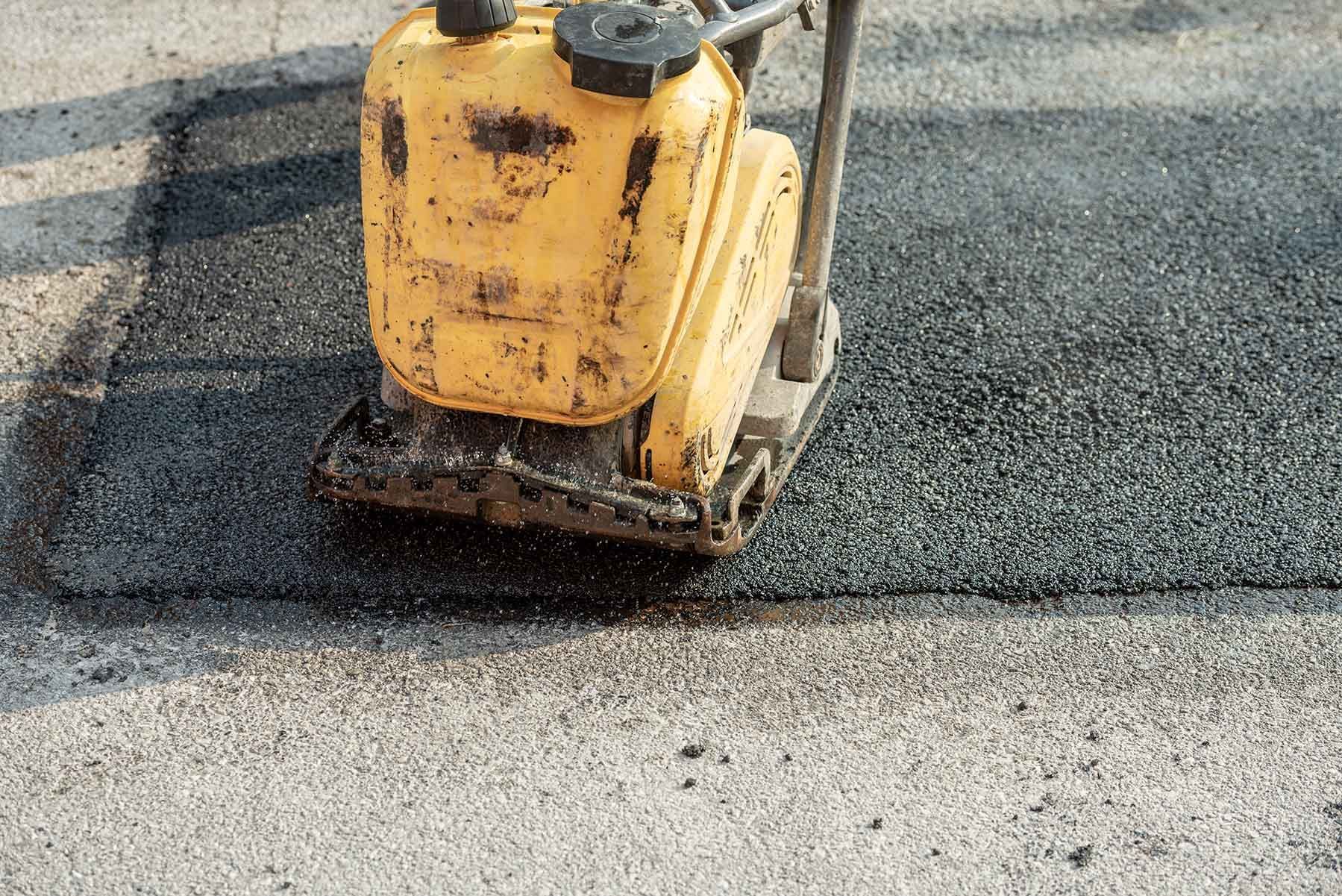 Yellow plate compactor showcasing asphalt resurfacing contractors at road repair site.