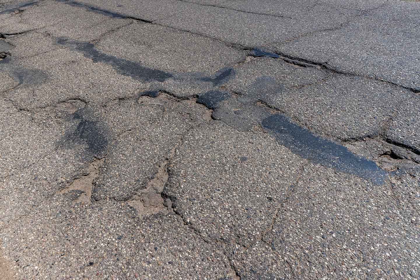 Damaged asphalt lot with cracks and patchwork areas needing resurfacing.