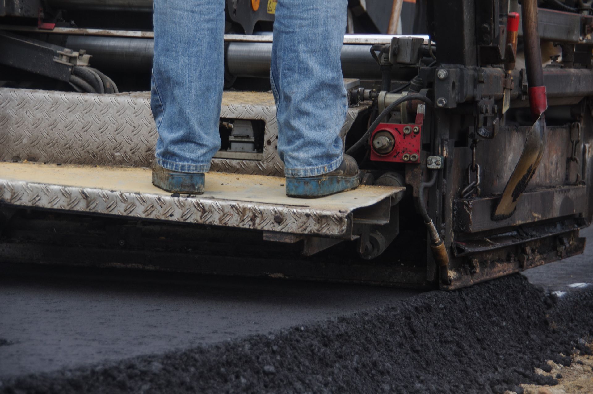 A worker operating an asphalt machine while paving a road, showcasing an asphalt paving contractor.