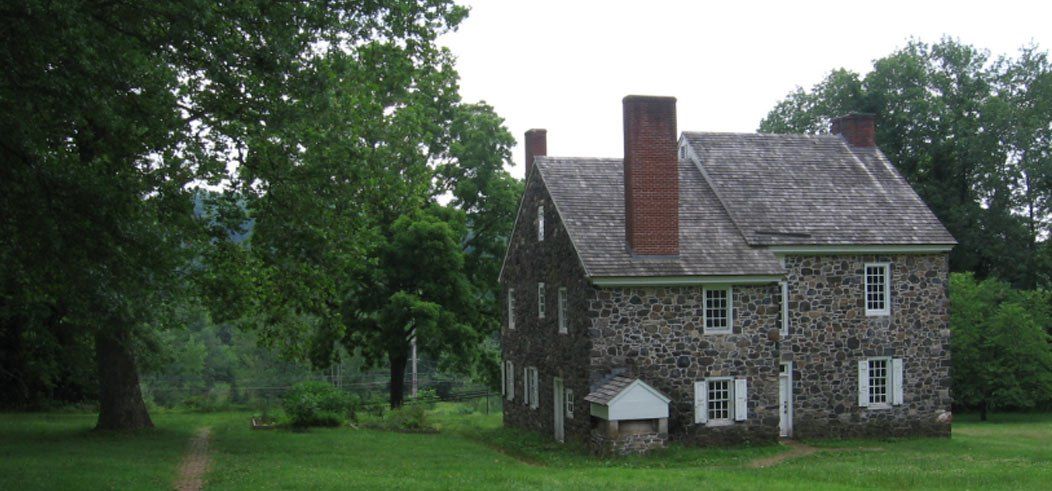 Stone house with red brick chimneys in a grassy field surrounded by trees.