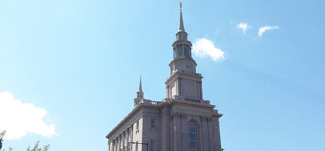 Tall stone building with a steeple against a clear blue sky, with a few clouds.
