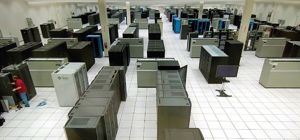 Data center with rows of computer servers. A person in a red shirt works on the equipment.