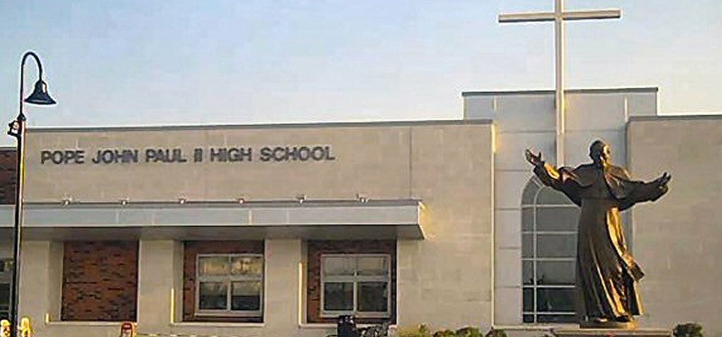 Pope John Paul II High School with a statue of the Pope and a large cross in front.