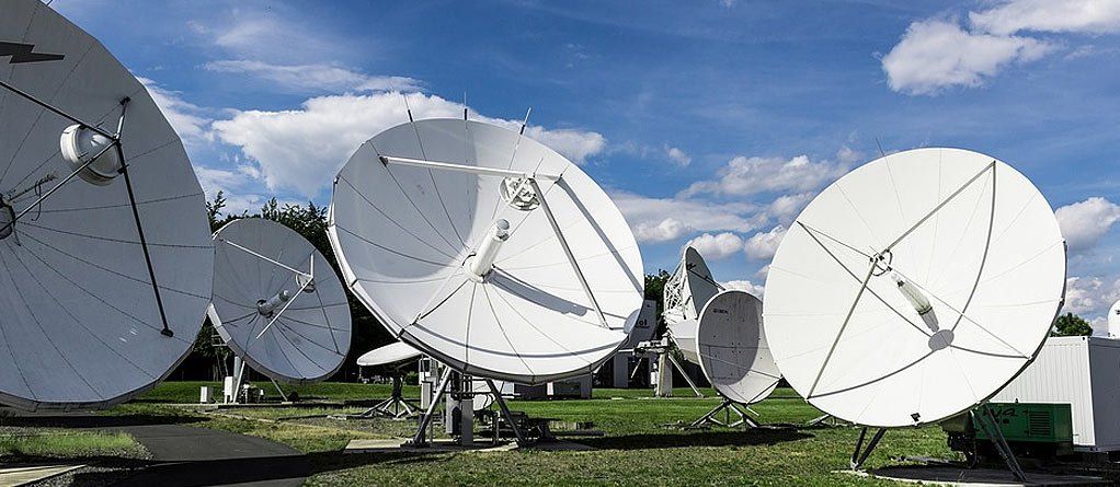A field of large satellite dishes against a blue sky with white clouds.