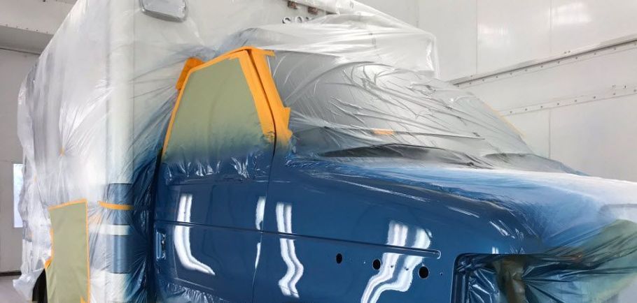 A blue van is being painted in a paint booth.