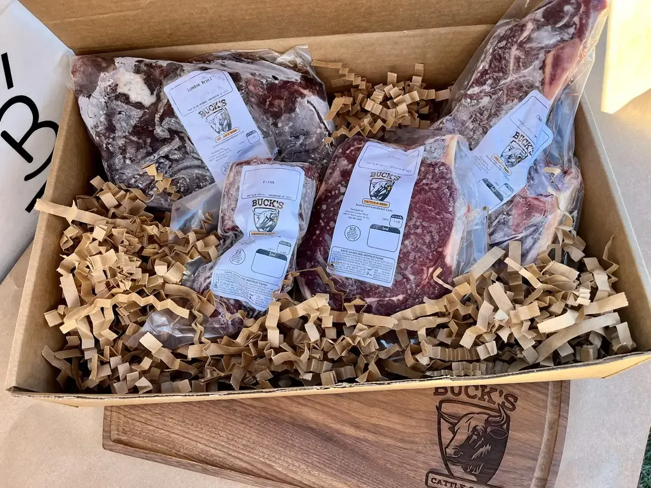 Gift box with shredded paper holding three vacuum-sealed cuts of meat with labels