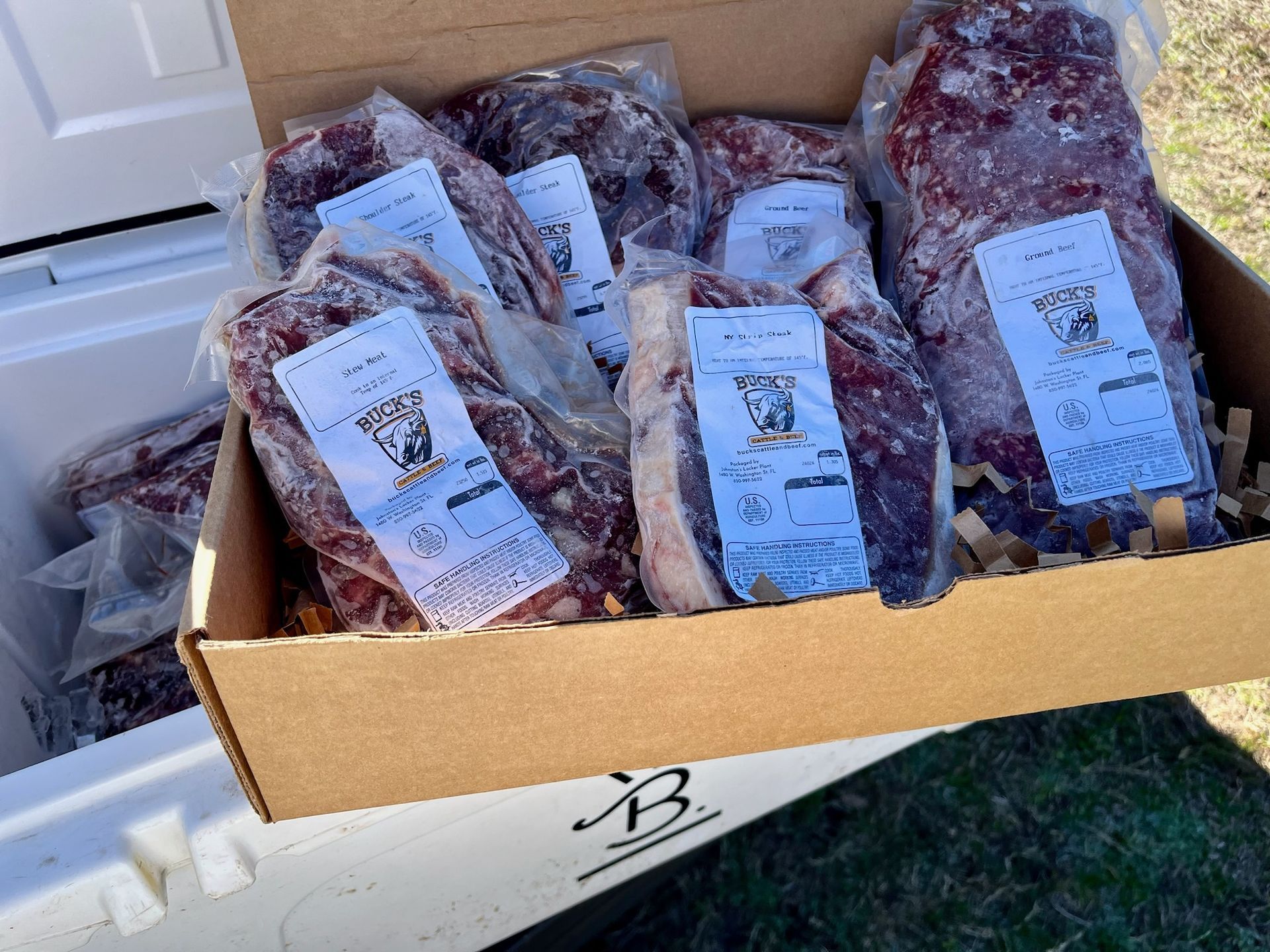 Open cardboard box filled with vacuum-sealed meat packages with white labels.