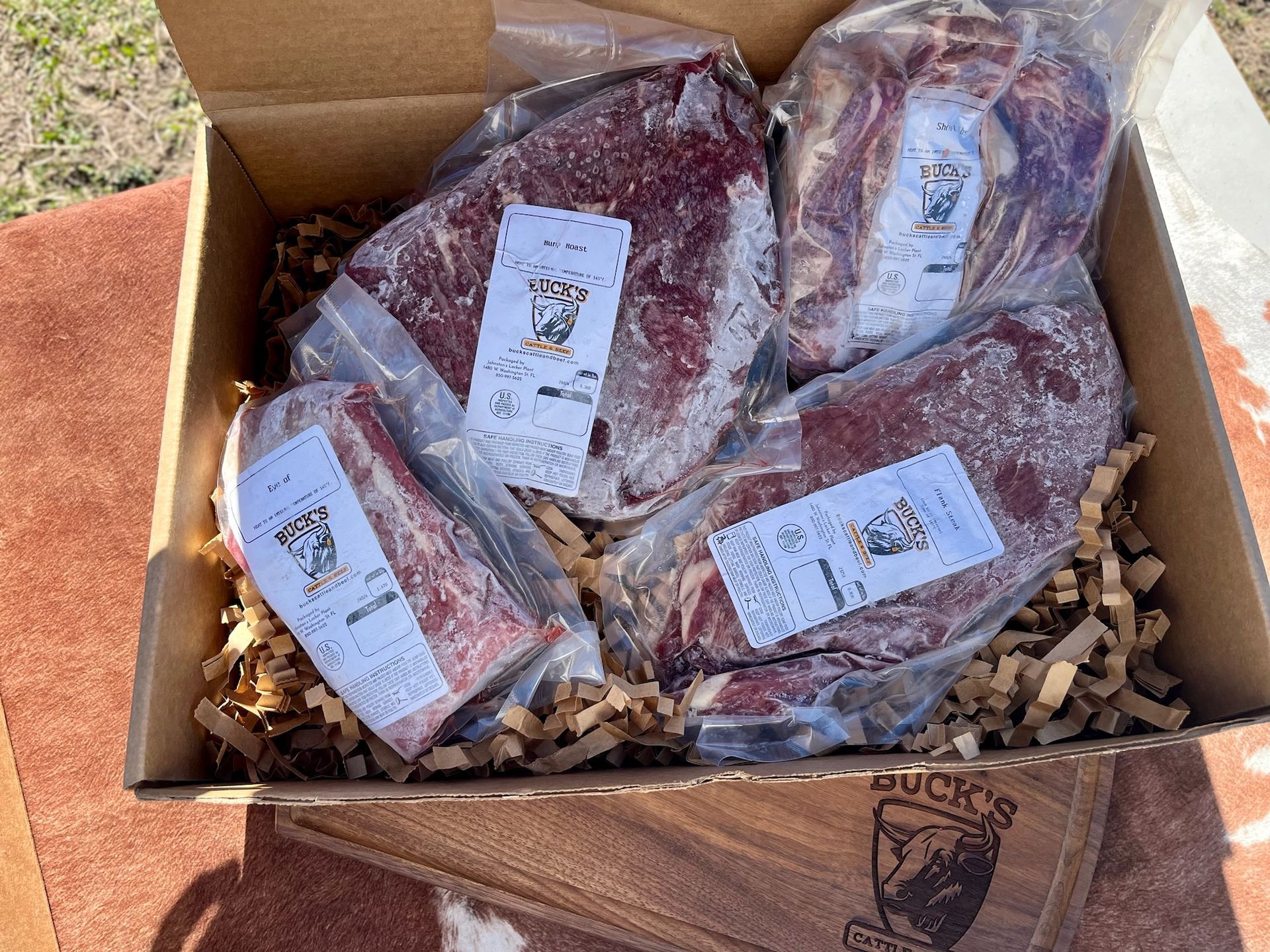 Open cardboard box with vacuum-sealed red meat packages on packing paper outdoors.