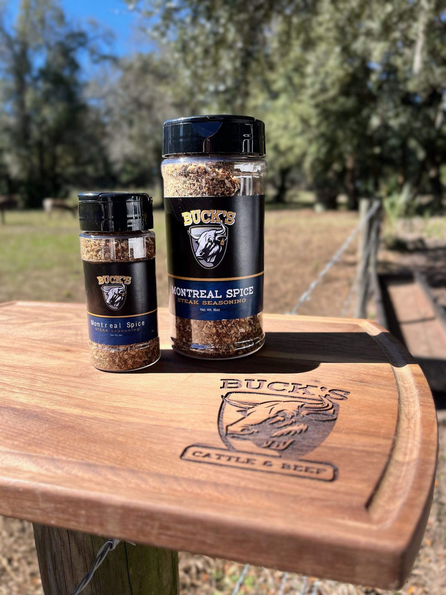 Two spice jars on a wooden cutting board outdoors, with trees blurred in the background.