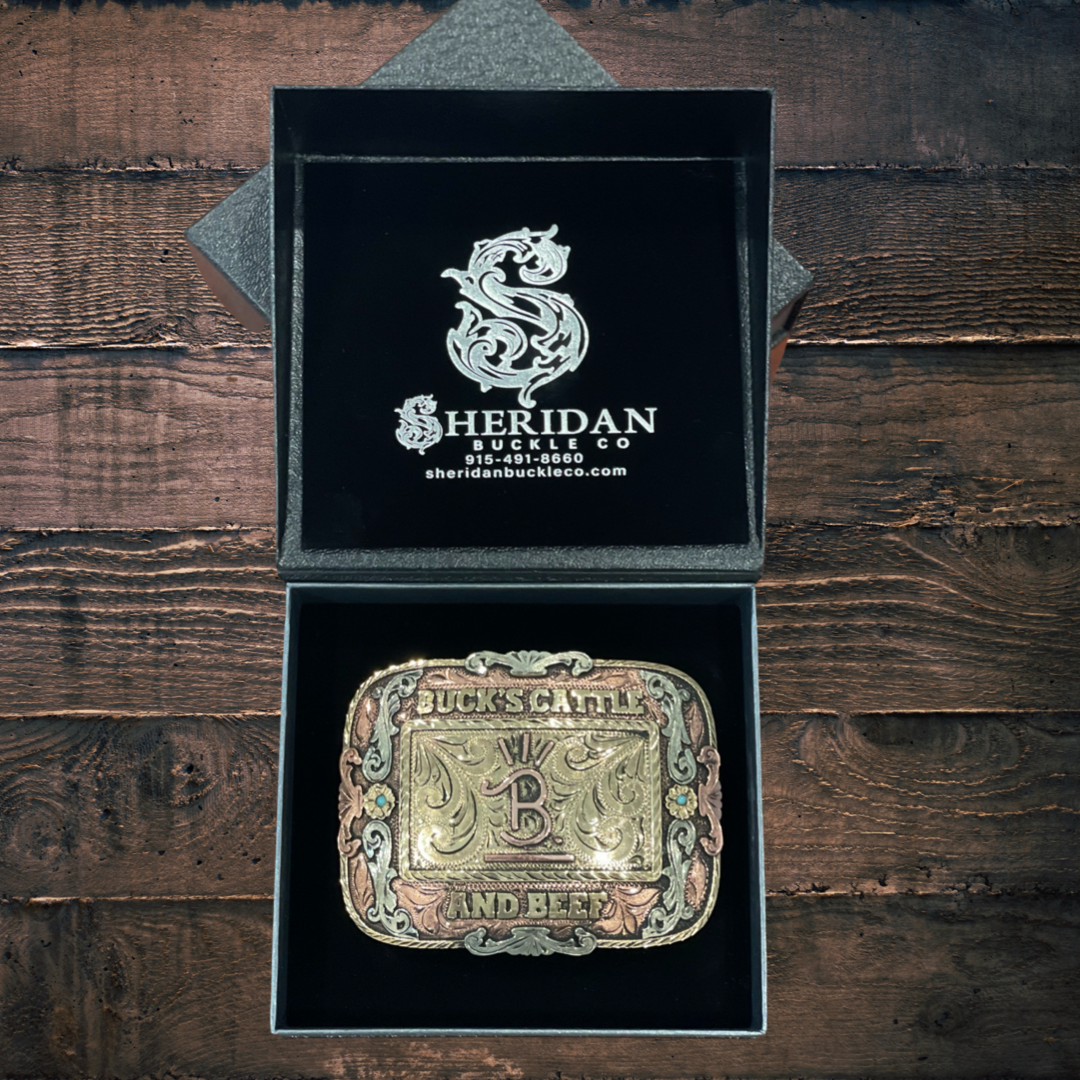 Black Sheridan box open on wooden surface, showing a decorative metal plaque inside.