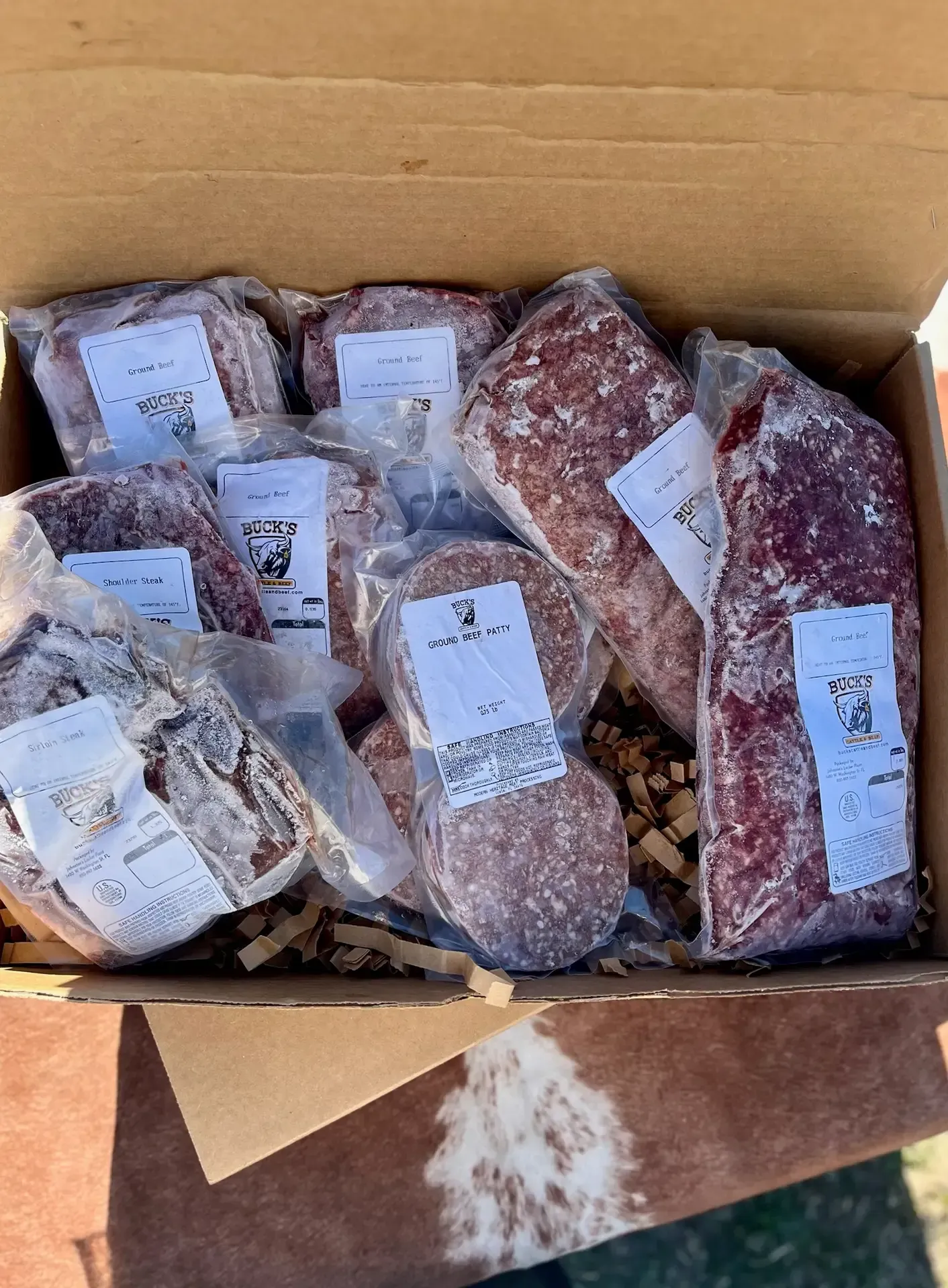 Open cardboard box filled with packaged cuts of meat in clear plastic with white labels.
