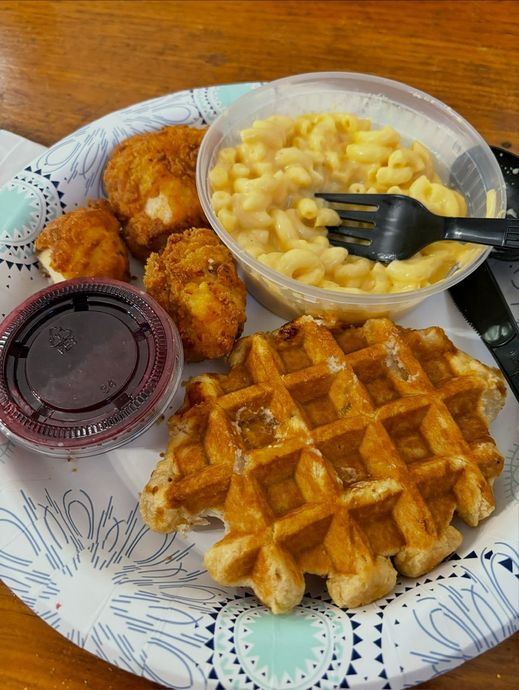 Plate with fried chicken bites, waffle with syrup, mac and cheese, and jelly cup.