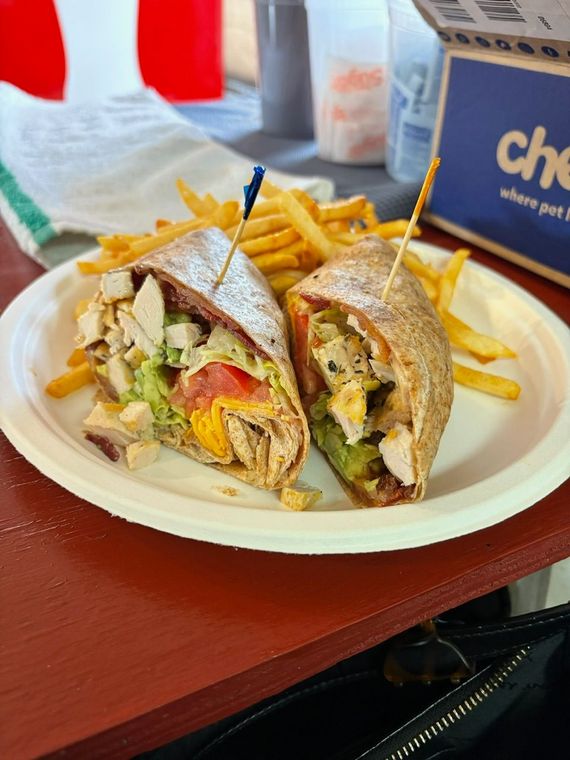Chicken wrap with fries on a white plate, wooden table, toothpicks, and Chewy box in the background.
