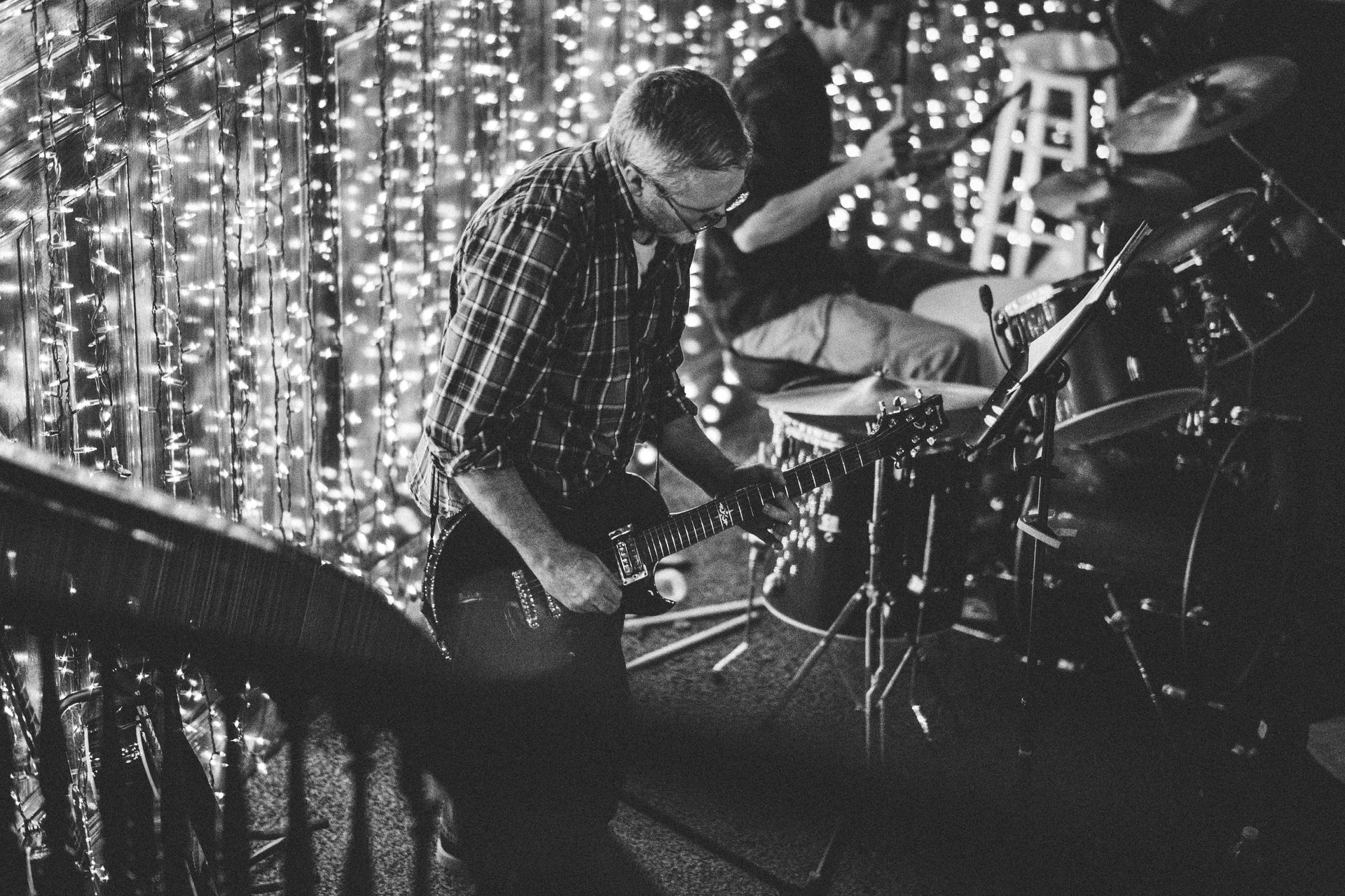 Black and white photo of a band playing on a stage decorated with string lights.