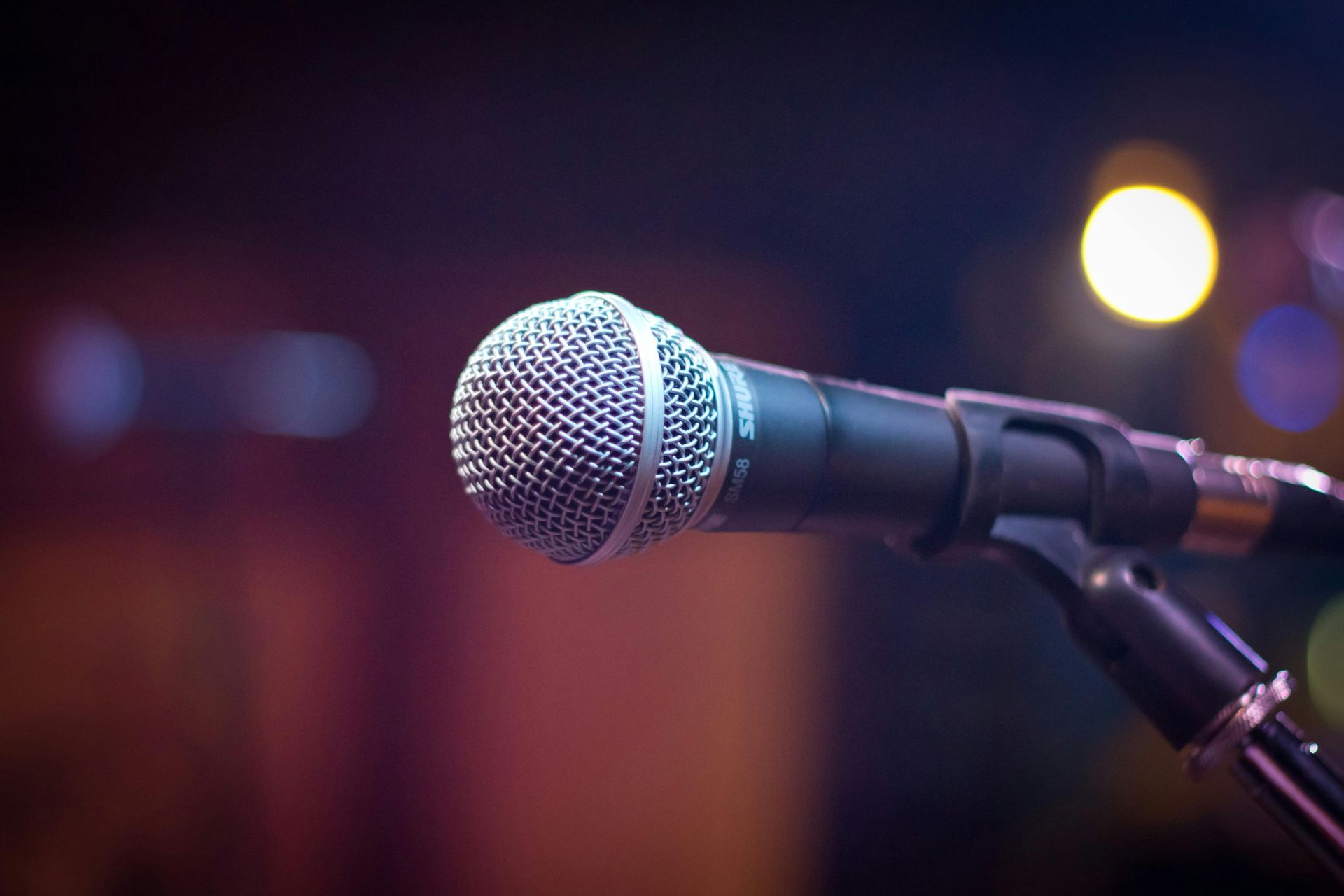 Microphone on stand, ready for performance in a dimly lit venue, stage lights in background.