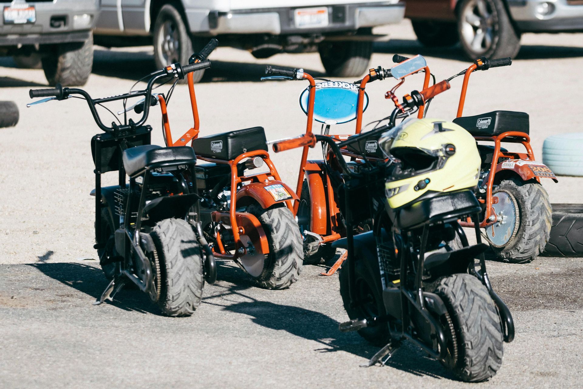Three orange and black mini bikes parked on asphalt with a yellow helmet hanging.
