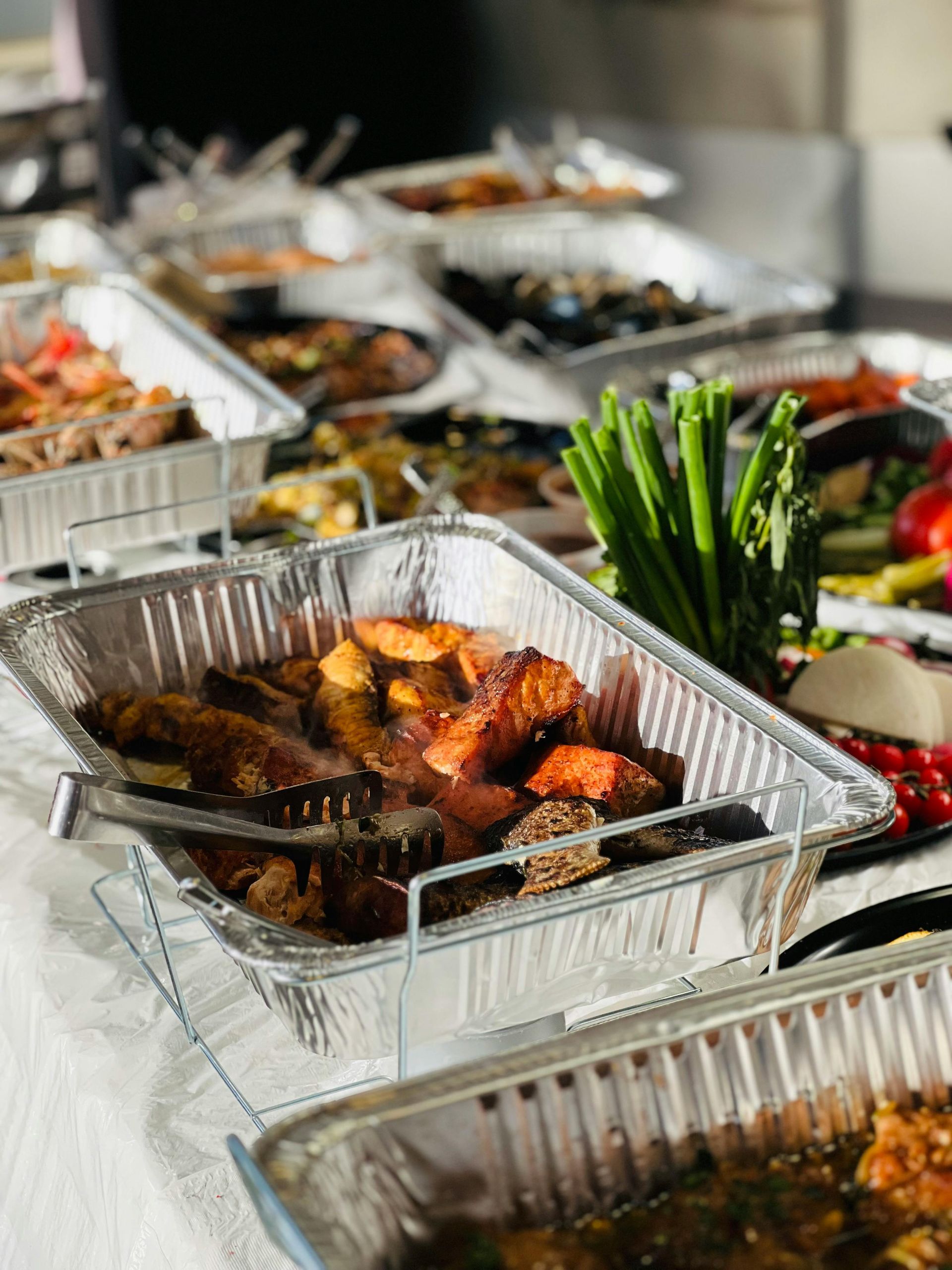 Buffet table with various dishes in aluminum trays, including vegetables and meats.