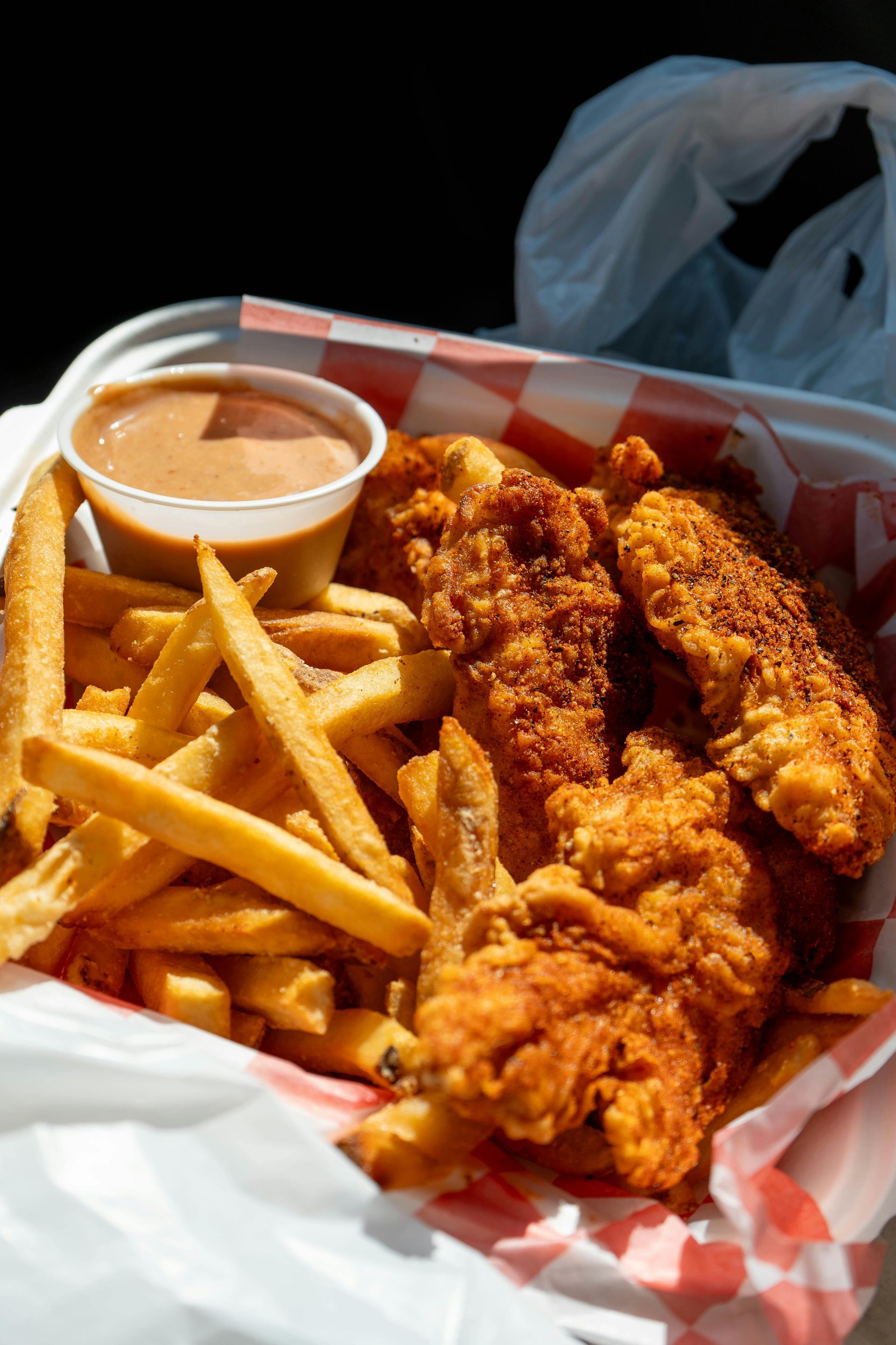 Fried chicken tenders and fries with dipping sauce in a to-go container.