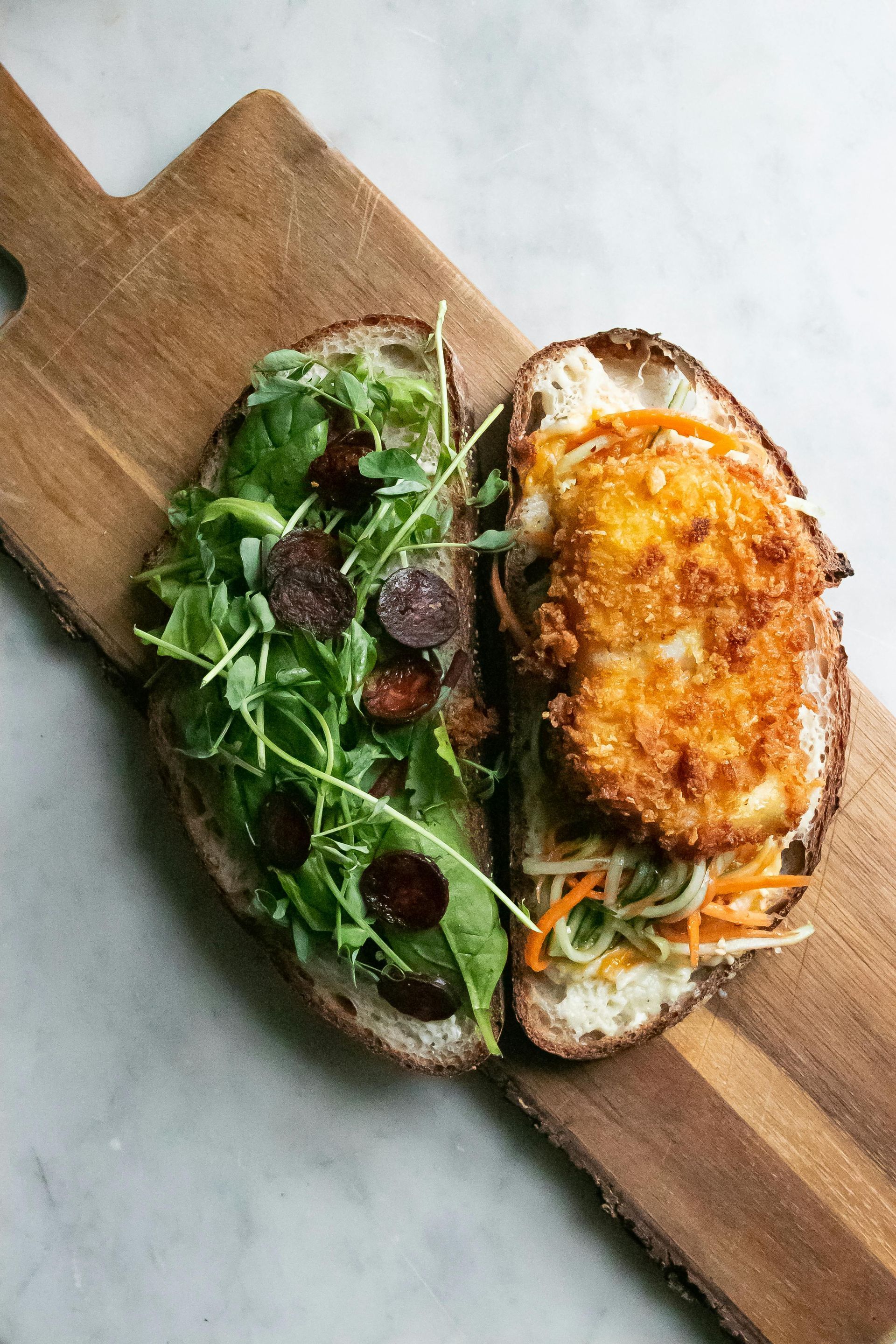 Open-faced sandwich: bread topped with arugula, beets, and a breaded cutlet and slaw. On a wooden board.