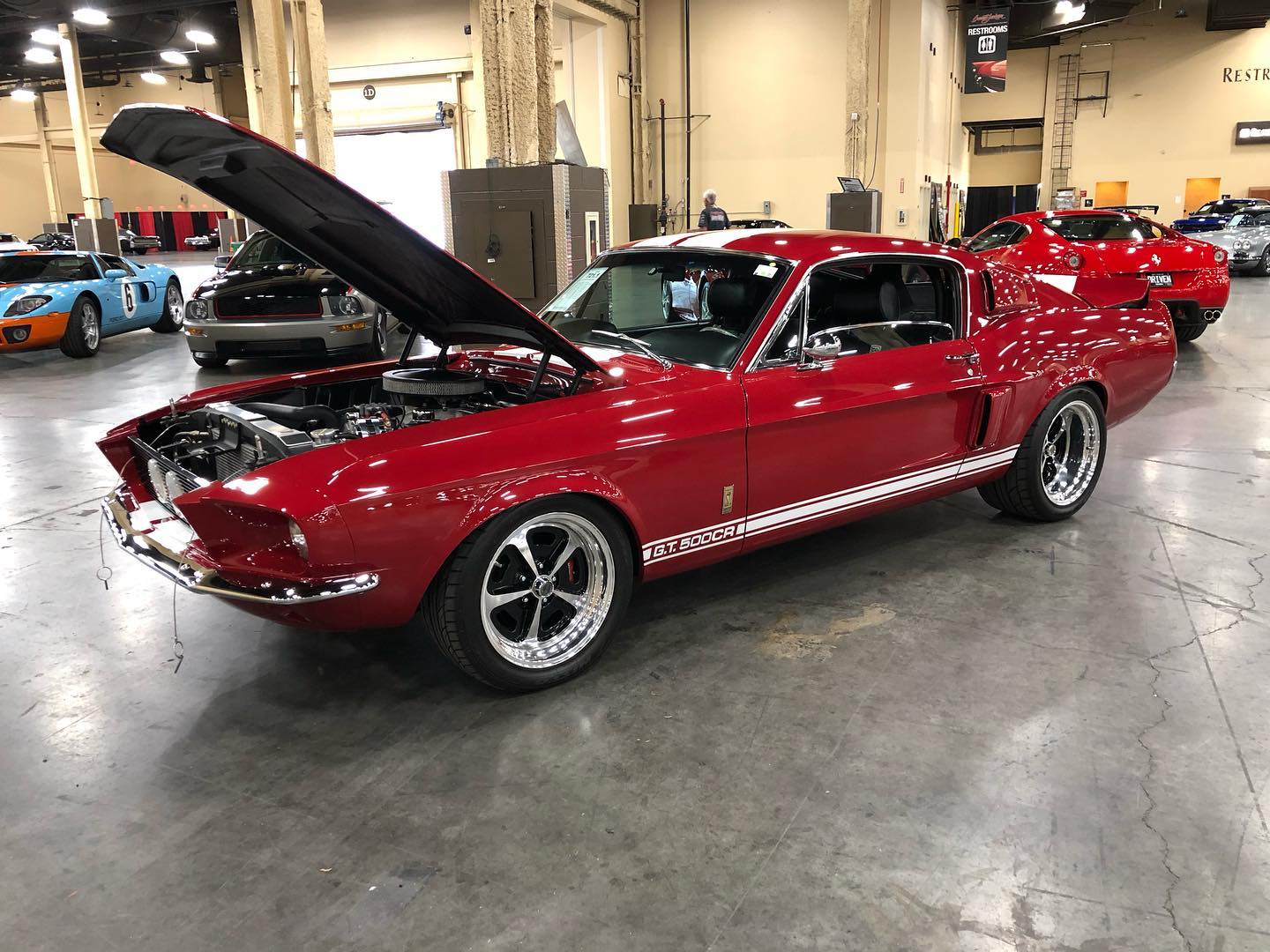 a red mustang with the hood up parked in a garage .