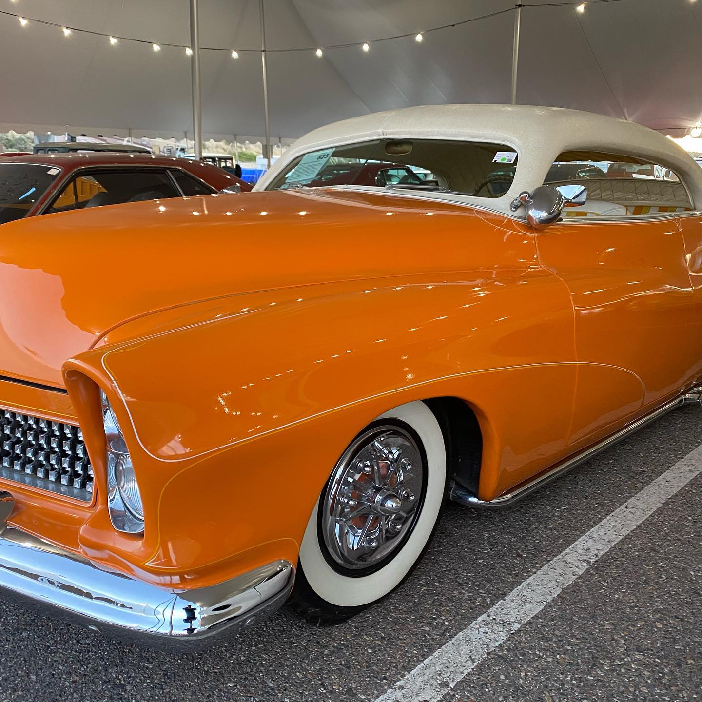 an orange car with white tires parked in a parking lot