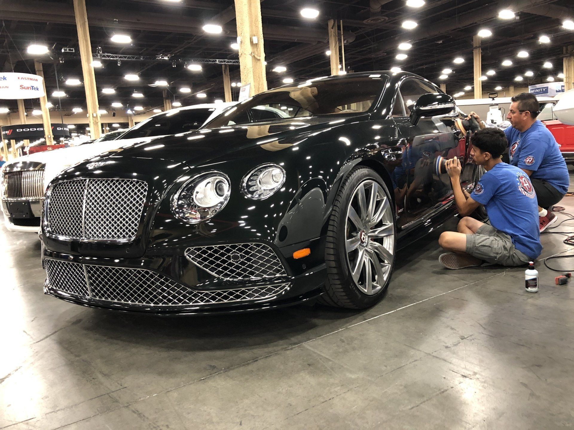two men are working on detailing a black bentley at a car show .