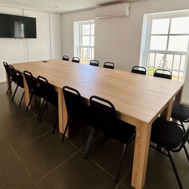 Conference room with long wood table and black chairs, TV on wall, and two windows.