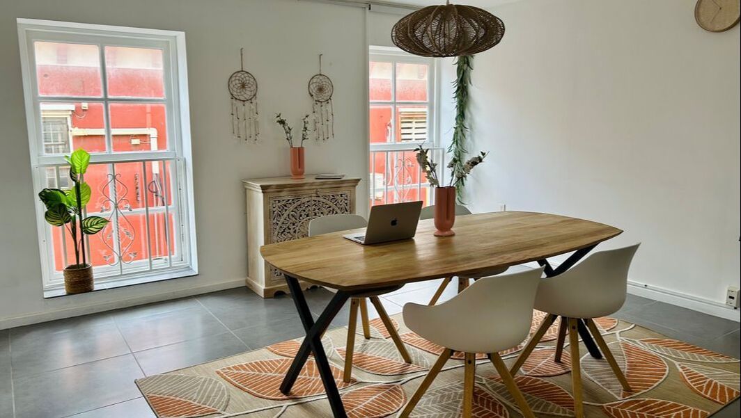 Dining room with a wooden table, white chairs, rug, and two windows.
