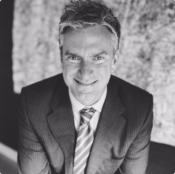 A man in a suit and tie is smiling in a black and white photo.