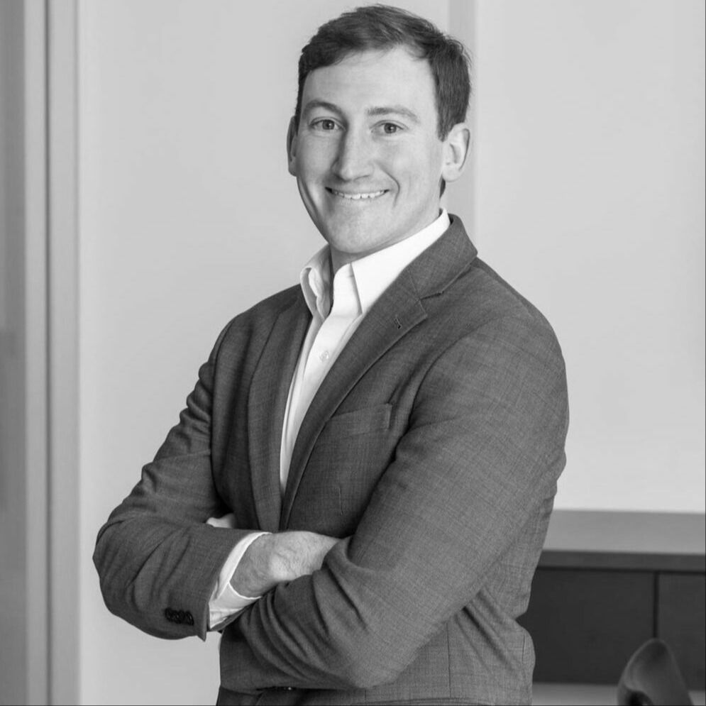 A man in a suit is smiling with his arms crossed in a black and white photo.