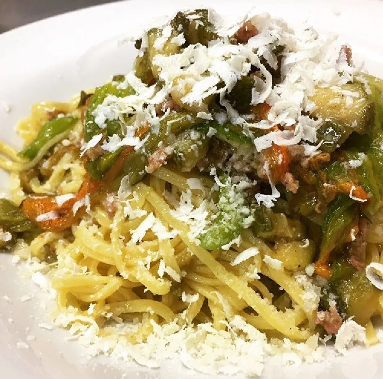 Un piatto di spaghetti con verdure e formaggio sopra