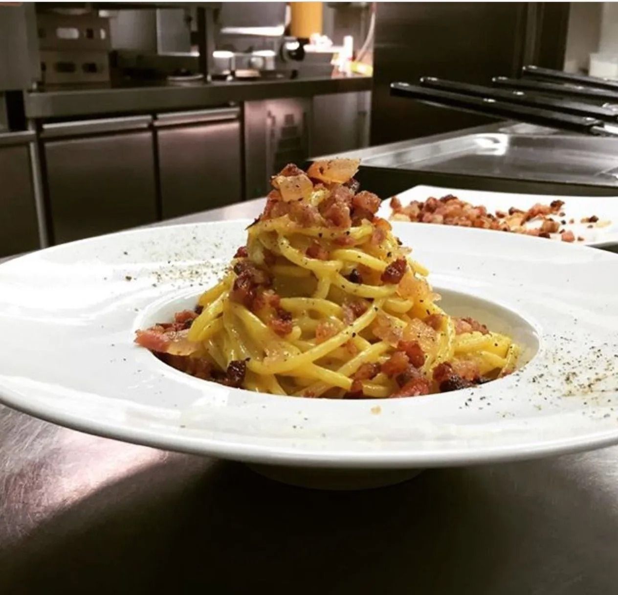 Un piatto bianco condito con spaghetti e pancetta