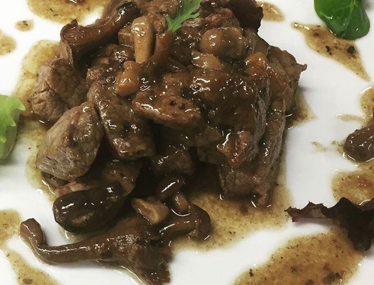 Un primo piano di un piatto di cibo con carne e funghi