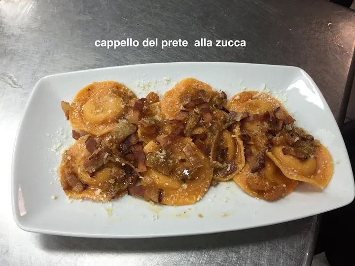 Un piatto bianco con ravioli e pancetta su un tavolo