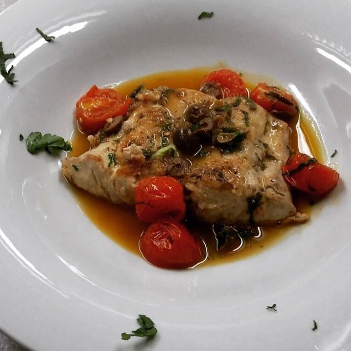 Un piatto bianco con pollo e pomodori