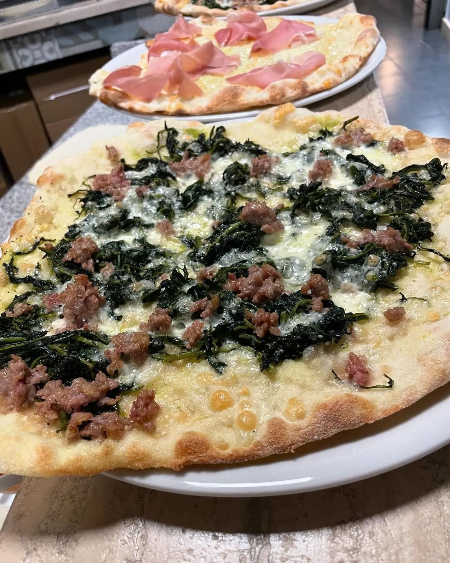 Una pizza con spinaci e carne su un piatto bianco su un tavolo.