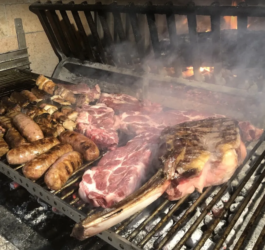 La carne e le salsicce vengono cotte su una griglia da cui esce del fumo.