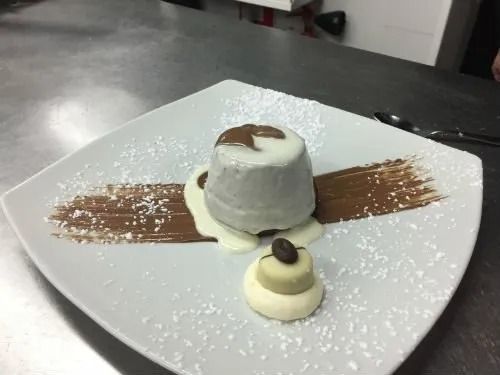 Un piatto bianco sormontato da un dessert con salsa al cioccolato e zucchero a velo.