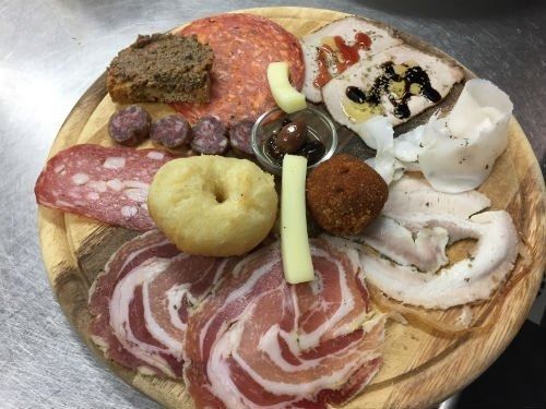 Un tagliere di legno sul quale vengono disposti vari tipi di carne e formaggi.