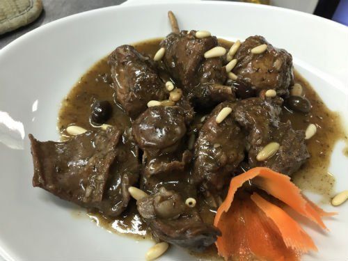 Un piatto bianco condito con carne e salsa con carote e pinoli.