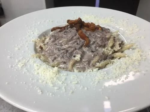 Un piatto bianco condito con pasta, formaggio e pancetta.