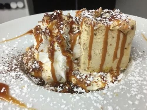 Un piatto bianco sormontato da un pezzo di dessert con panna montata e salsa al caramello.