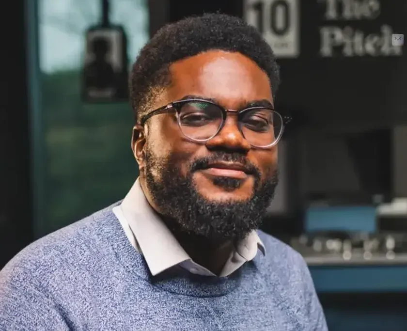 Man with glasses smiling, wearing a blue sweater, indoors.