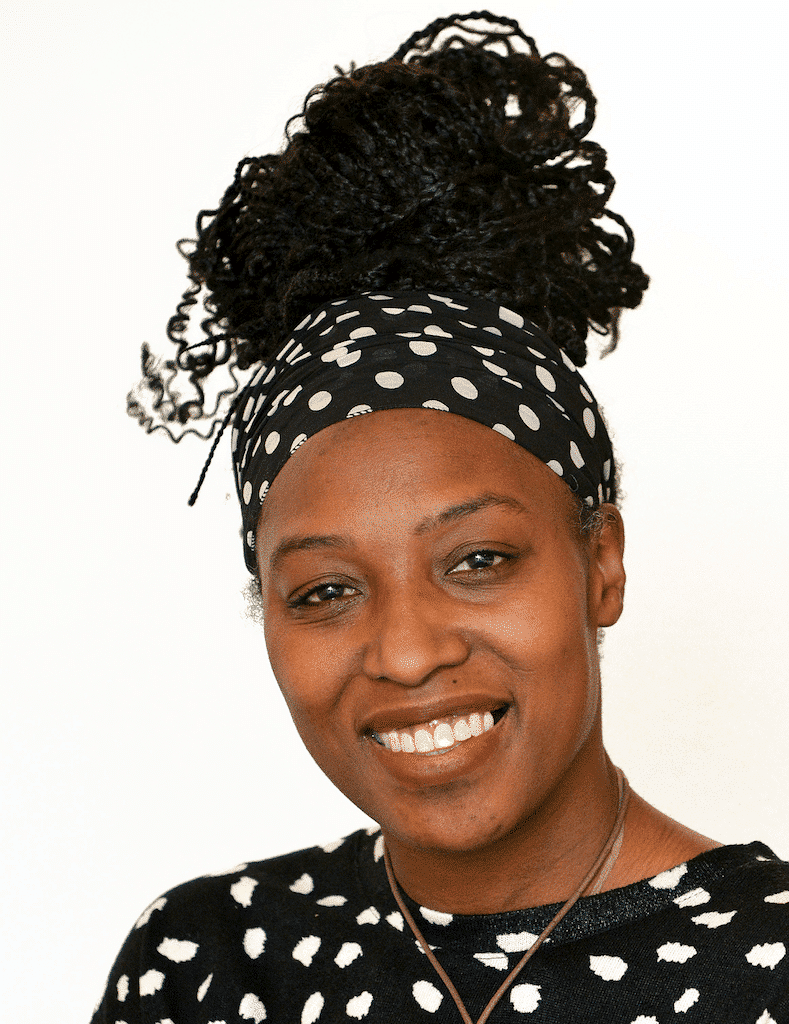 Black woman with dark curly hair, smiling, wearing a polka dot head wrap and sweater.