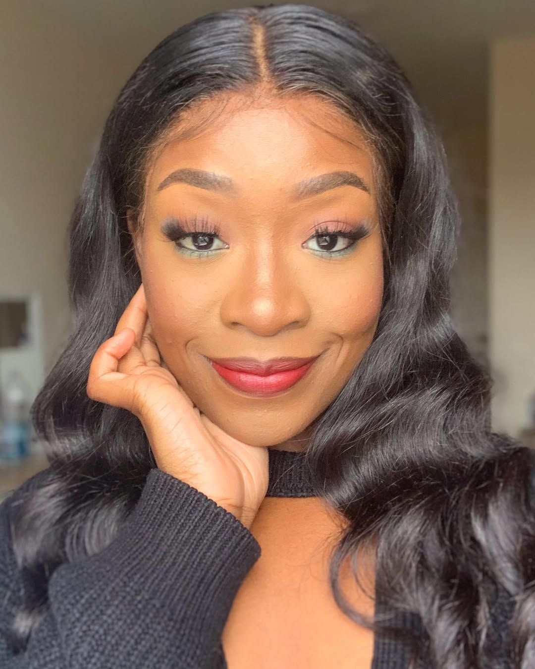 Black woman with wavy black hair, smiling, wearing a dark sweater.