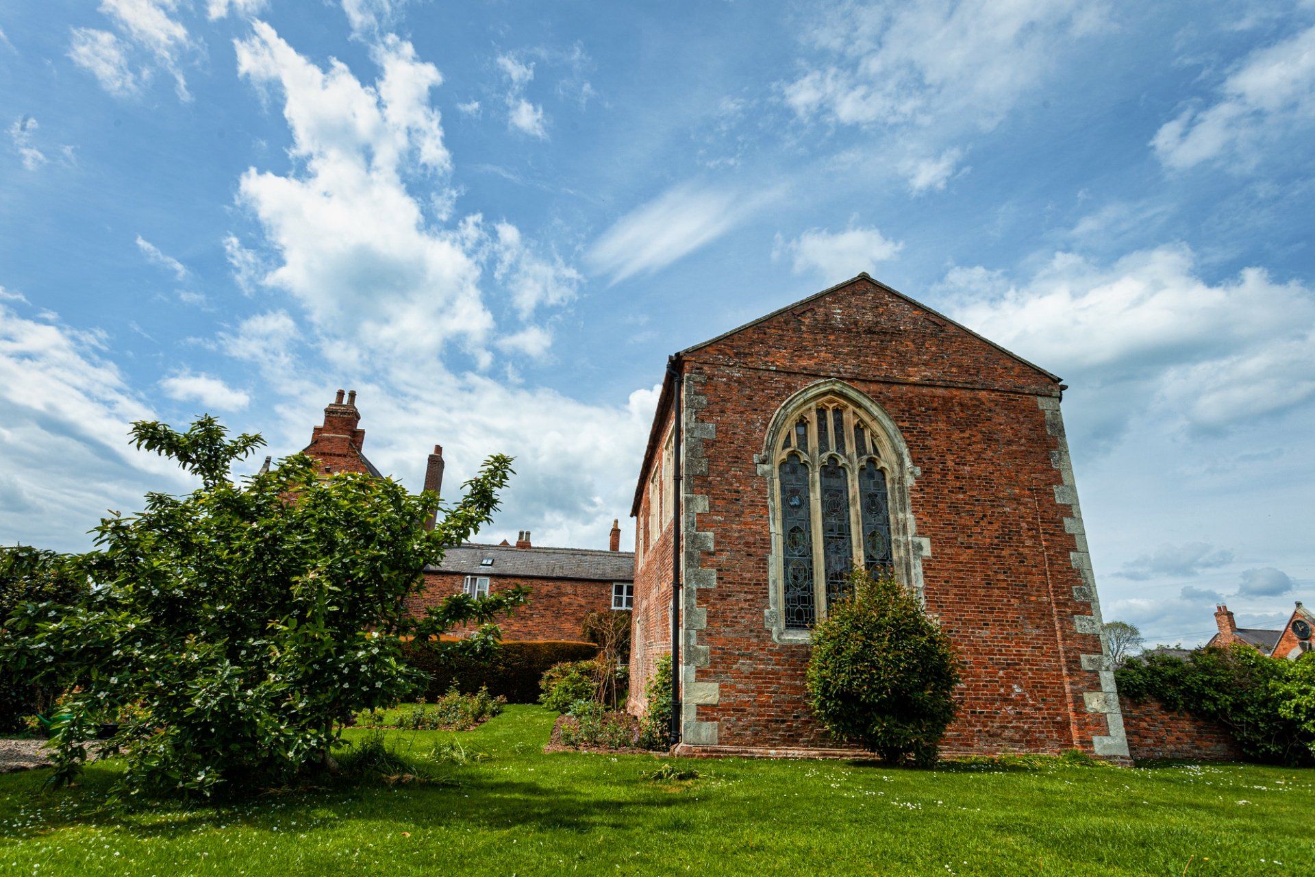 A brick building with a large window is sitting in the middle of a lush green field.