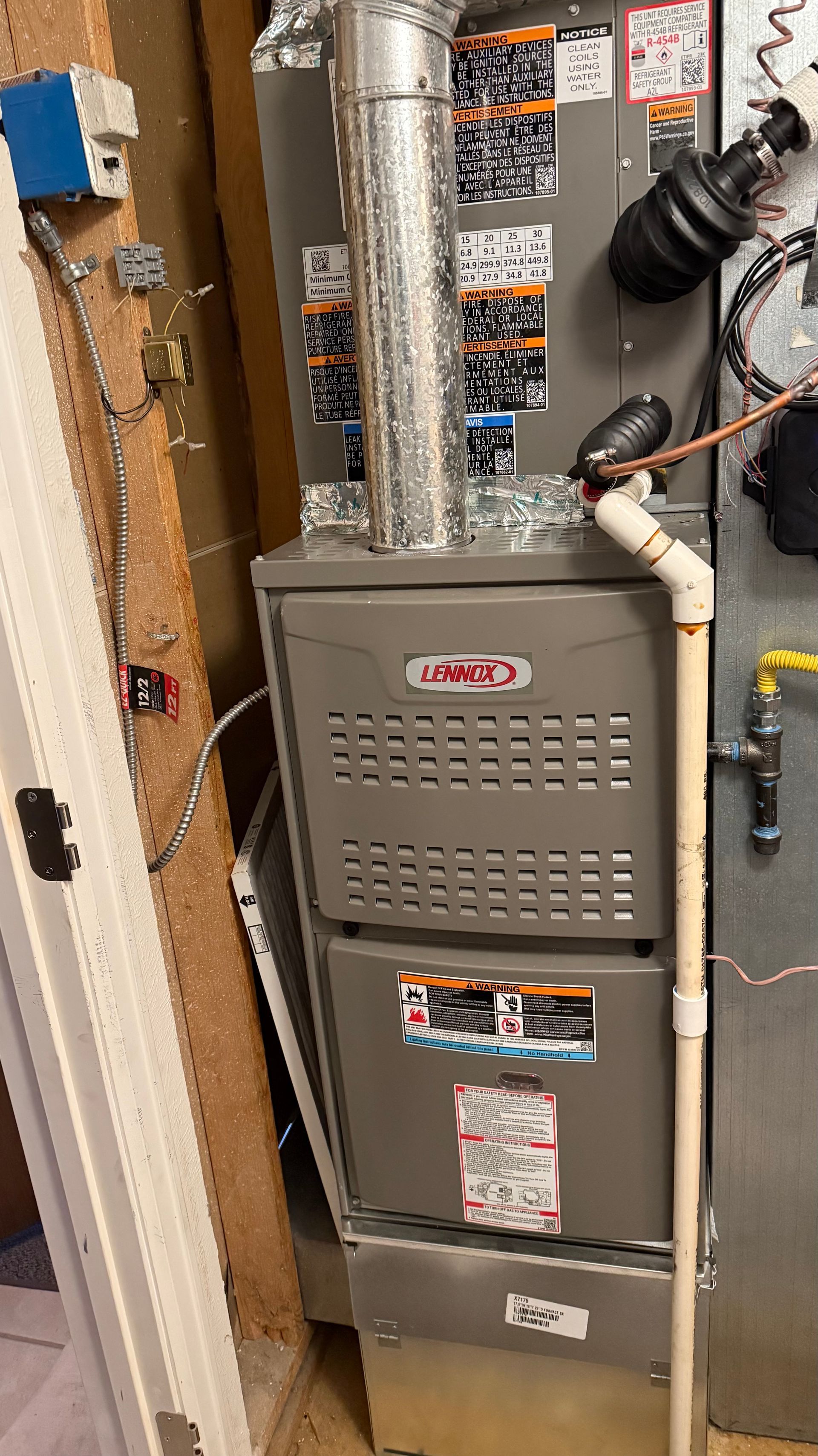 A Lennox furnace with a silver vent pipe. It's installed in a utility room with exposed wires and a gas line.
