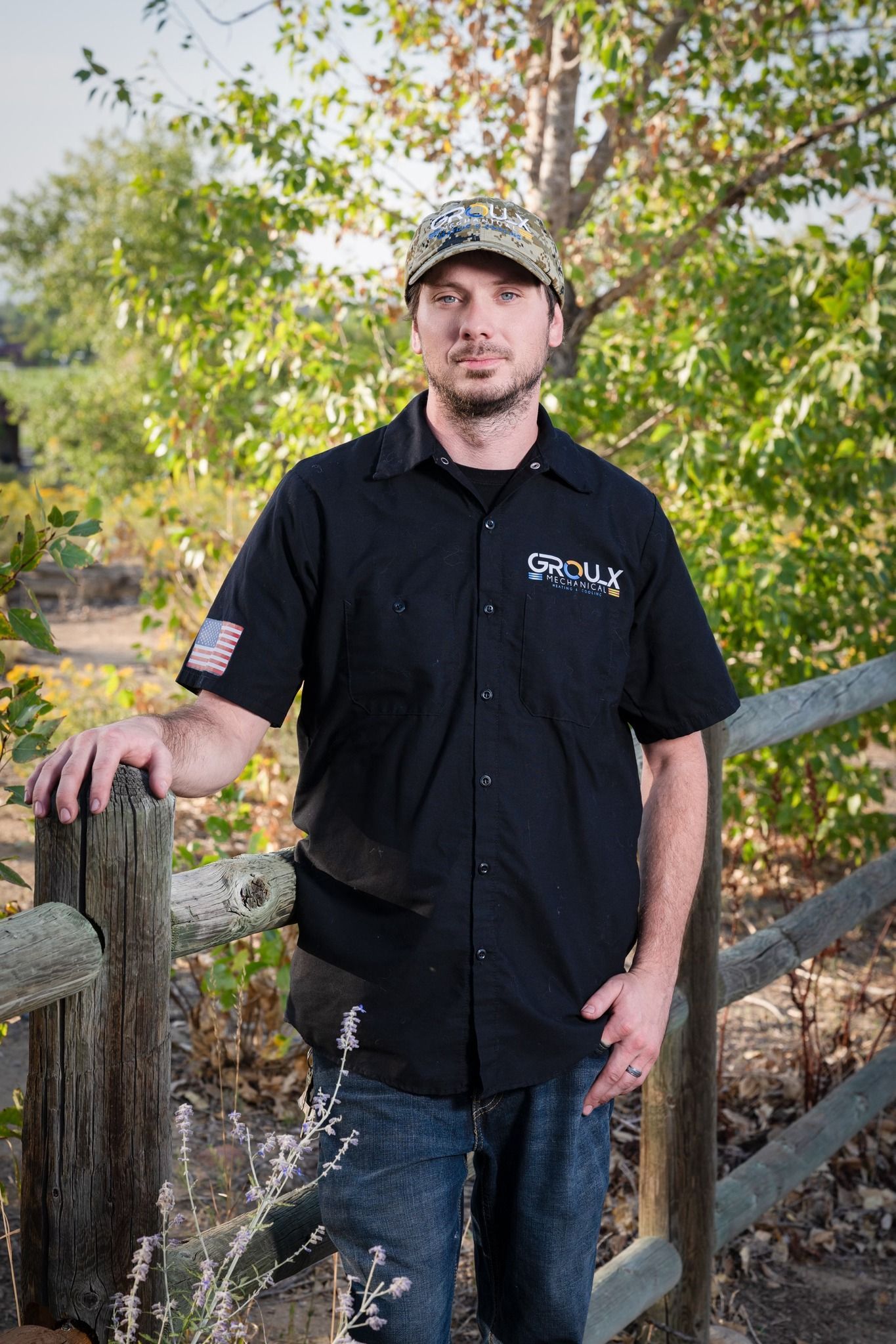 A man in a black shirt and hat is leaning on a wooden fence post.