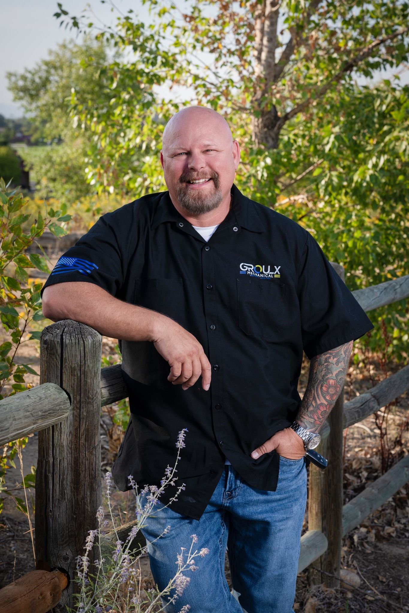 A man in a black shirt is leaning against a wooden fence.