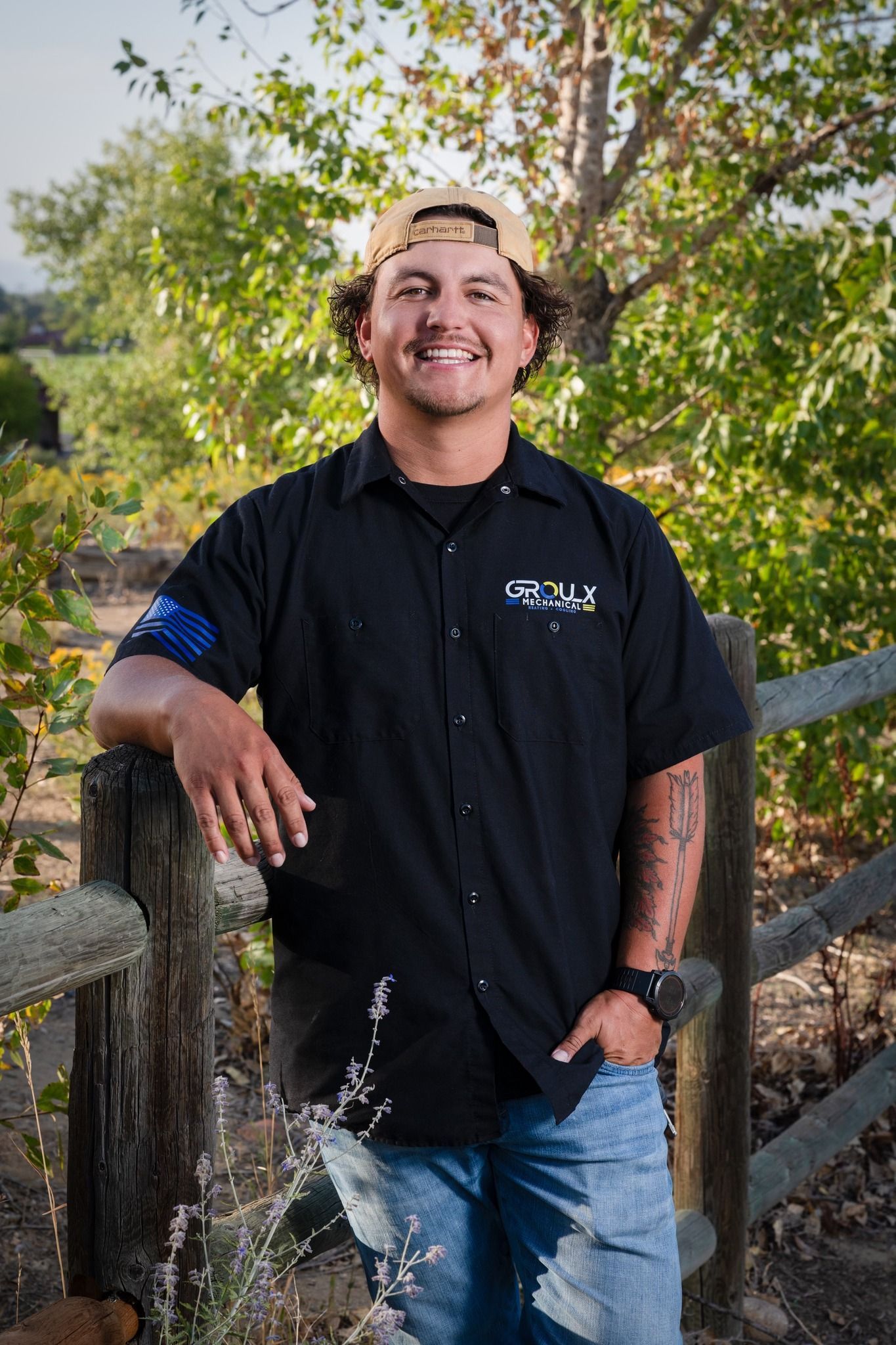 A man in a black shirt and hat is standing next to a wooden fence.